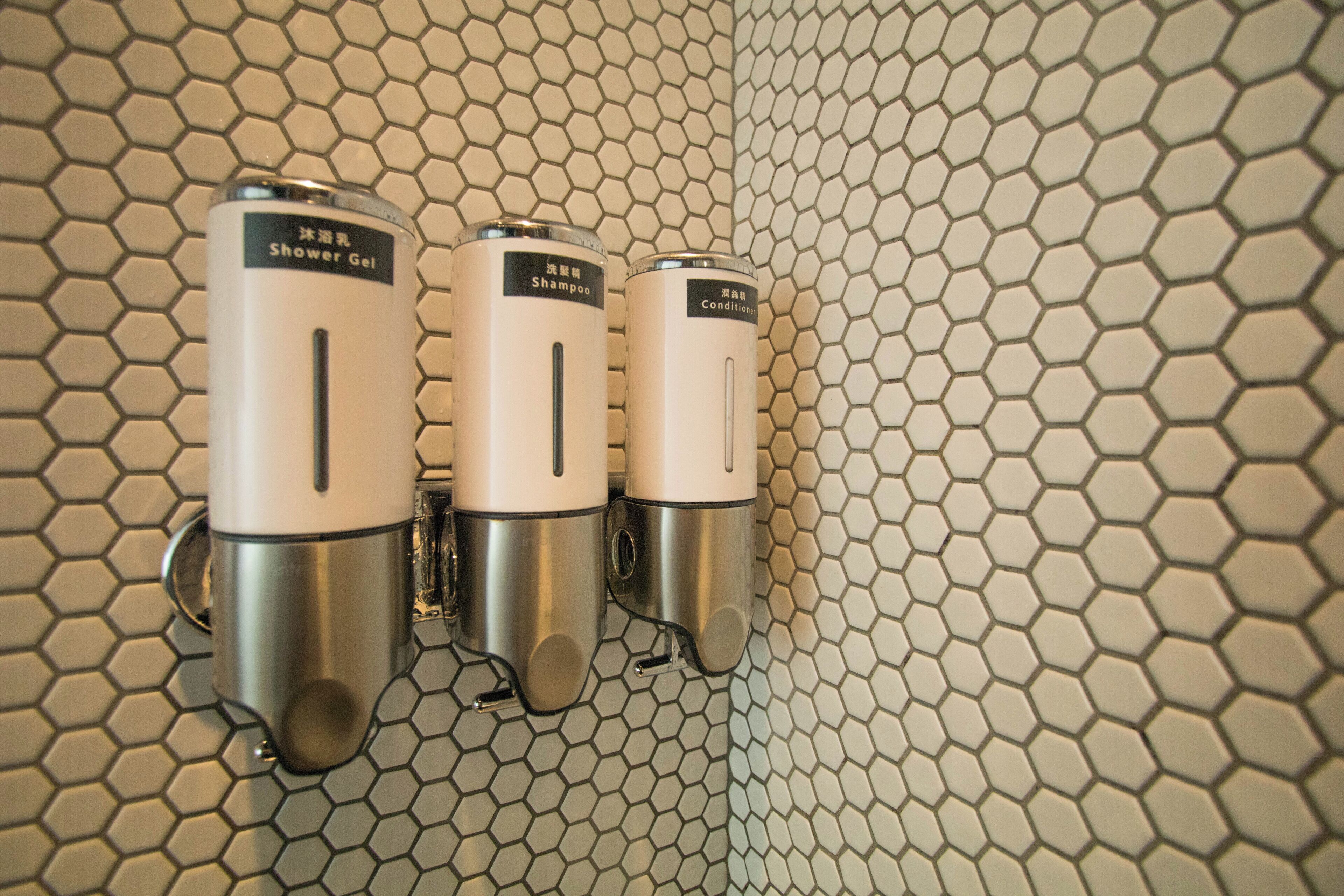 Three wall-mounted dispensers for shower gel, shampoo, and conditioner.