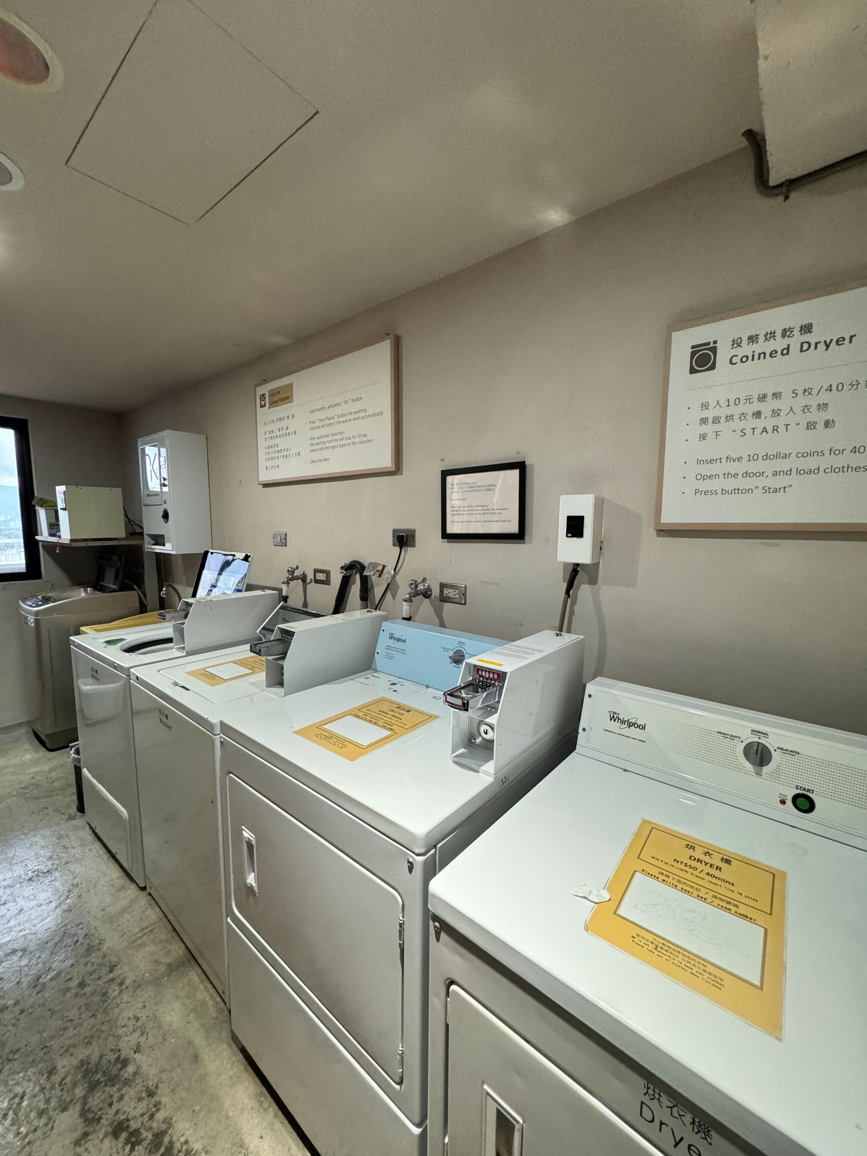 A laundry facility with multiple washing machines and dryers, instructional signs, and a Whirlpool brand dryer.