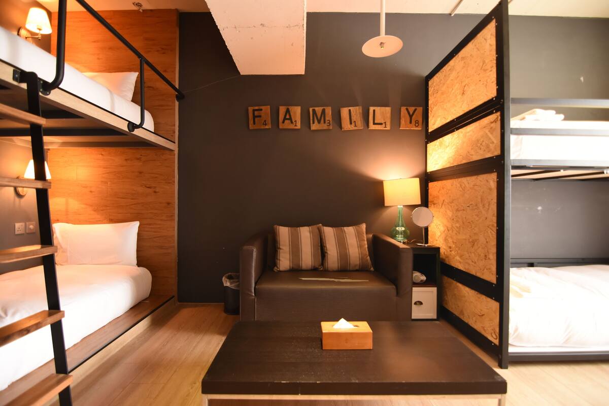 A compact room with bunk beds, a sofa, a small table, and a wall-mounted lamp.