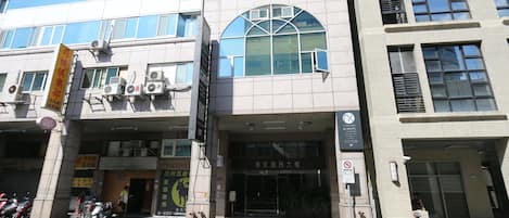A multi-story building with a large arched window on the ground floor, a signboard, and a no-smoking sign.