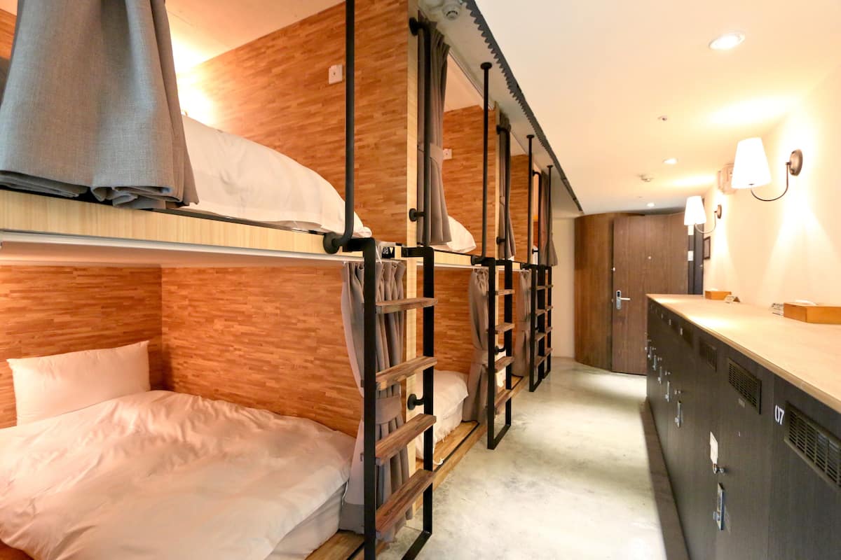 A bunk bed room with a wooden wall, a desk with a lamp, and a door in the background.