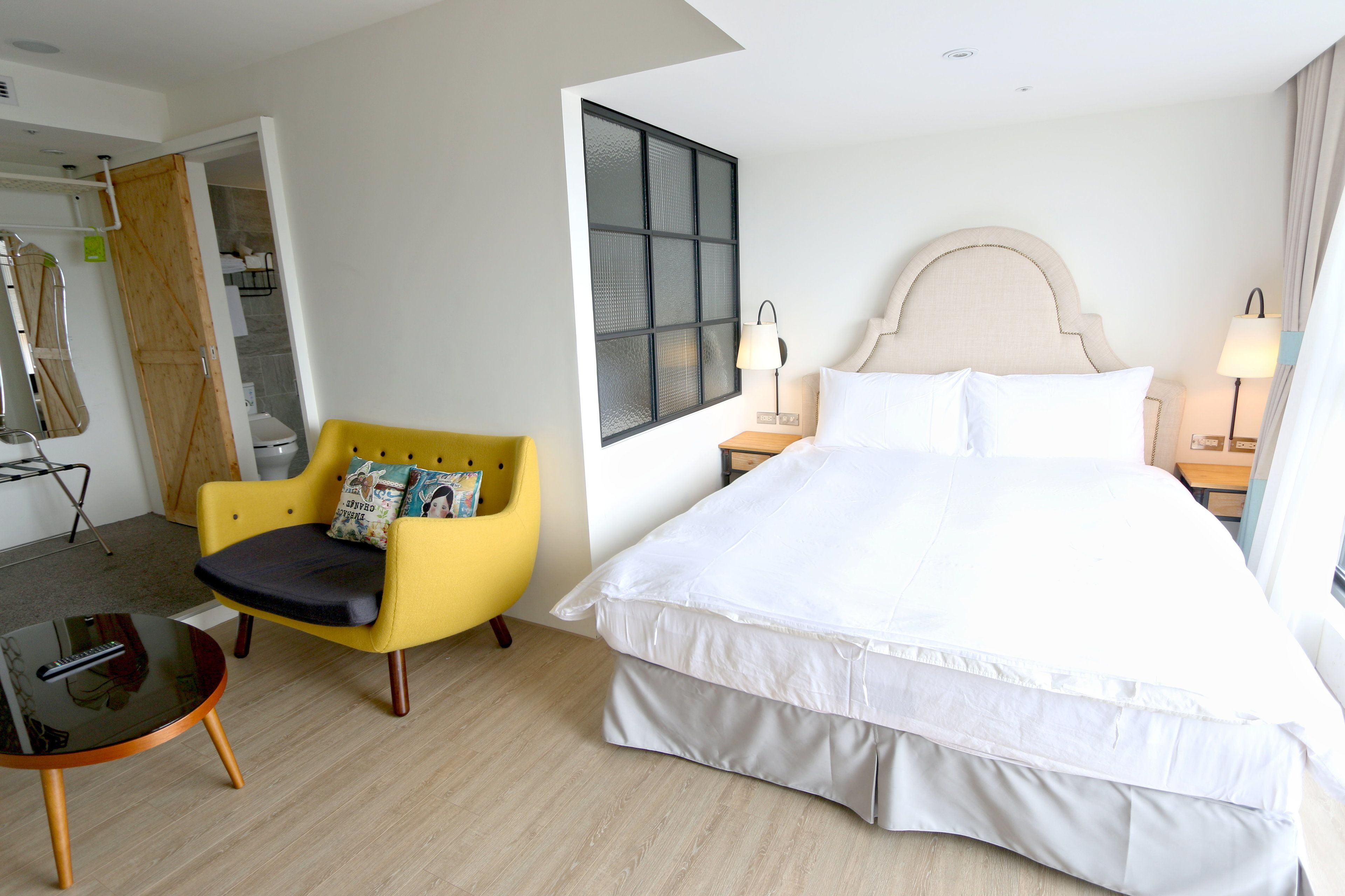 Habitación de hotel con una cama grande, un sillón amarillo, una mesita y una ventana con vistas.