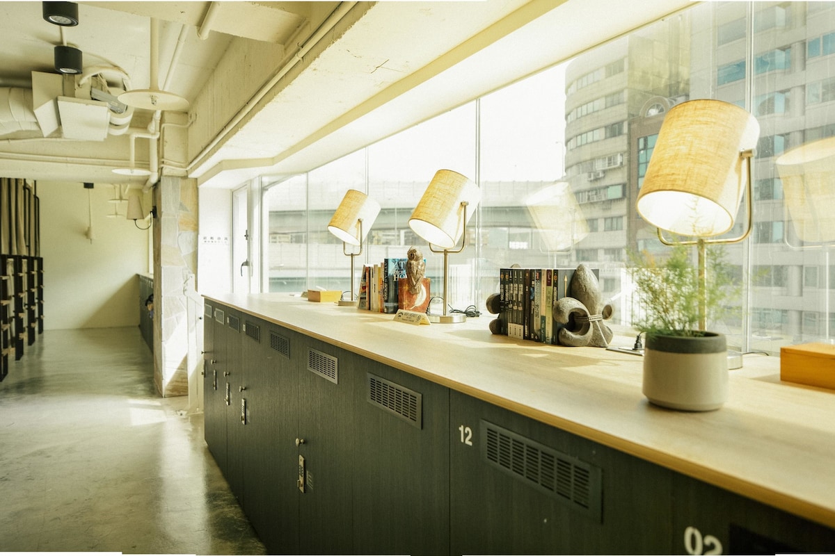 Une chambre d’hôtel moderne avec une grande fenêtre, un comptoir en bois agrémenté d’une plante et une vue sur le paysage urbain.