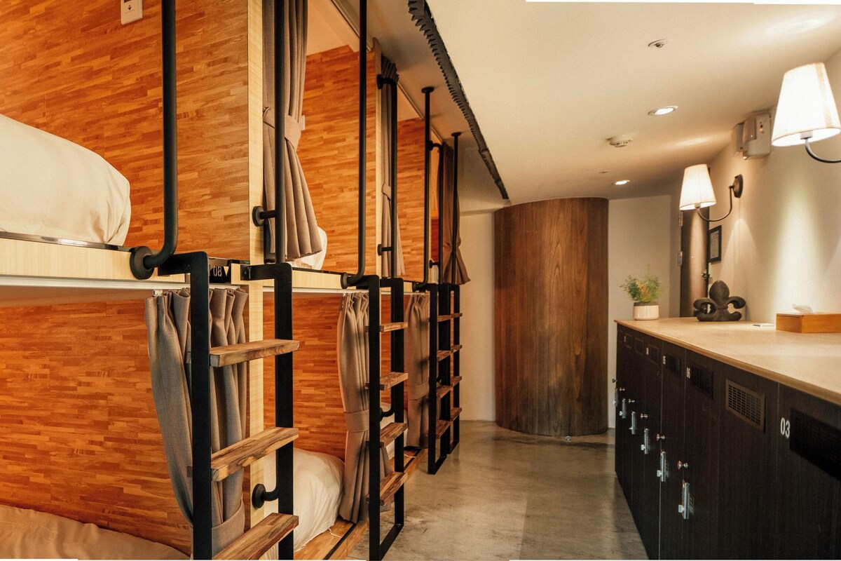Une chambre avec un lit superposé doté de têtes de lit en bois, une kitchenette avec un plan de travail en bois et une lampe fixée au mur.