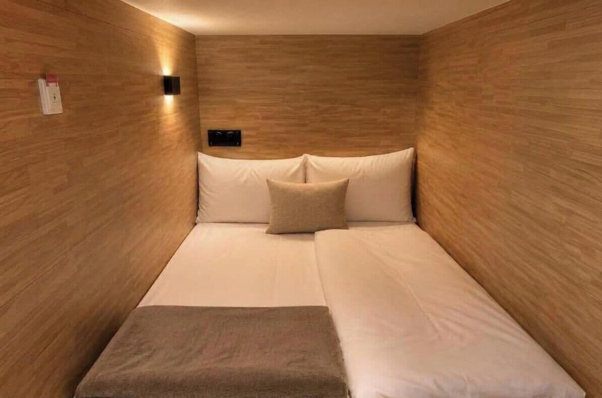 A room with a bed, a bedside table, and a wall-mounted light fixture.
