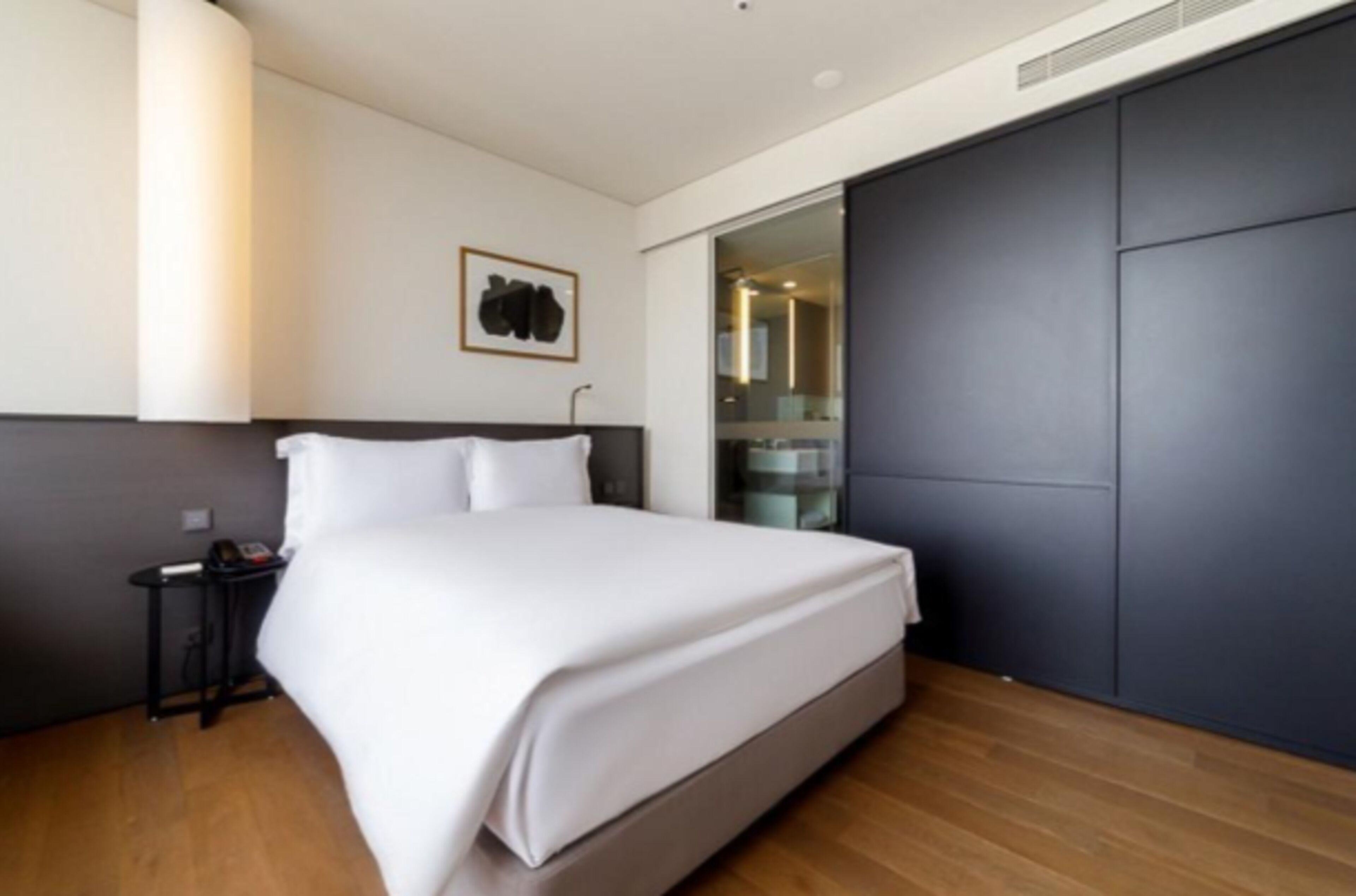 A modern bedroom with a large bed, a bedside table, a wall-mounted light, and a sliding door closet.