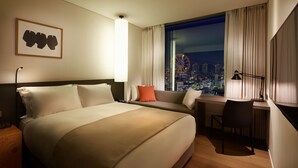 Habitación de hotel con una cama grande, un escritorio y una silla. Se ve una ventana con vistas a la ciudad.
