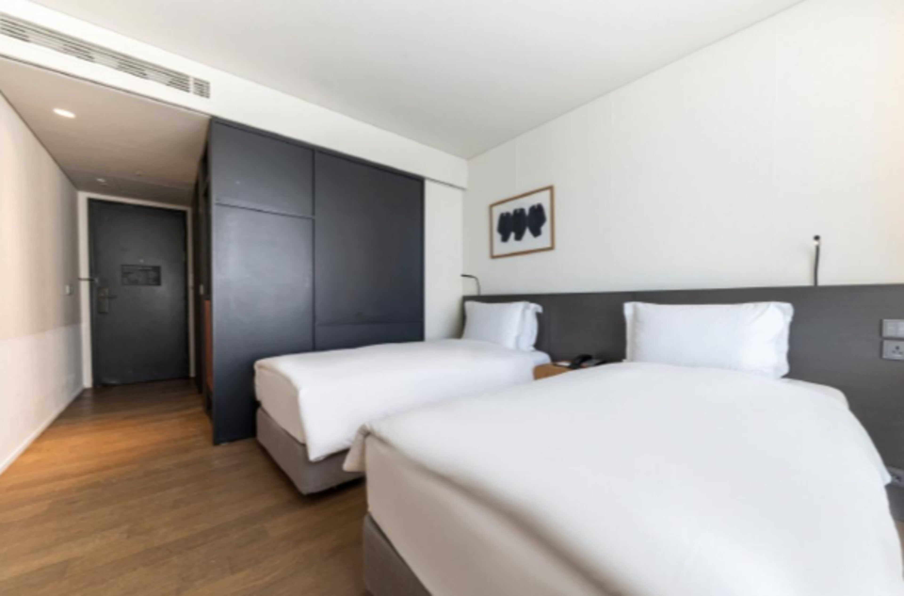 Una habitación de hotel moderna con dos camas, un armario oscuro y un cuadro enmarcado en la pared.