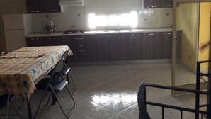 A compact kitchen with dark cabinets, a gas stove, and a sink. There is a dining table with chairs and a window providing natural light. - Case Corona (Santa Flavia)