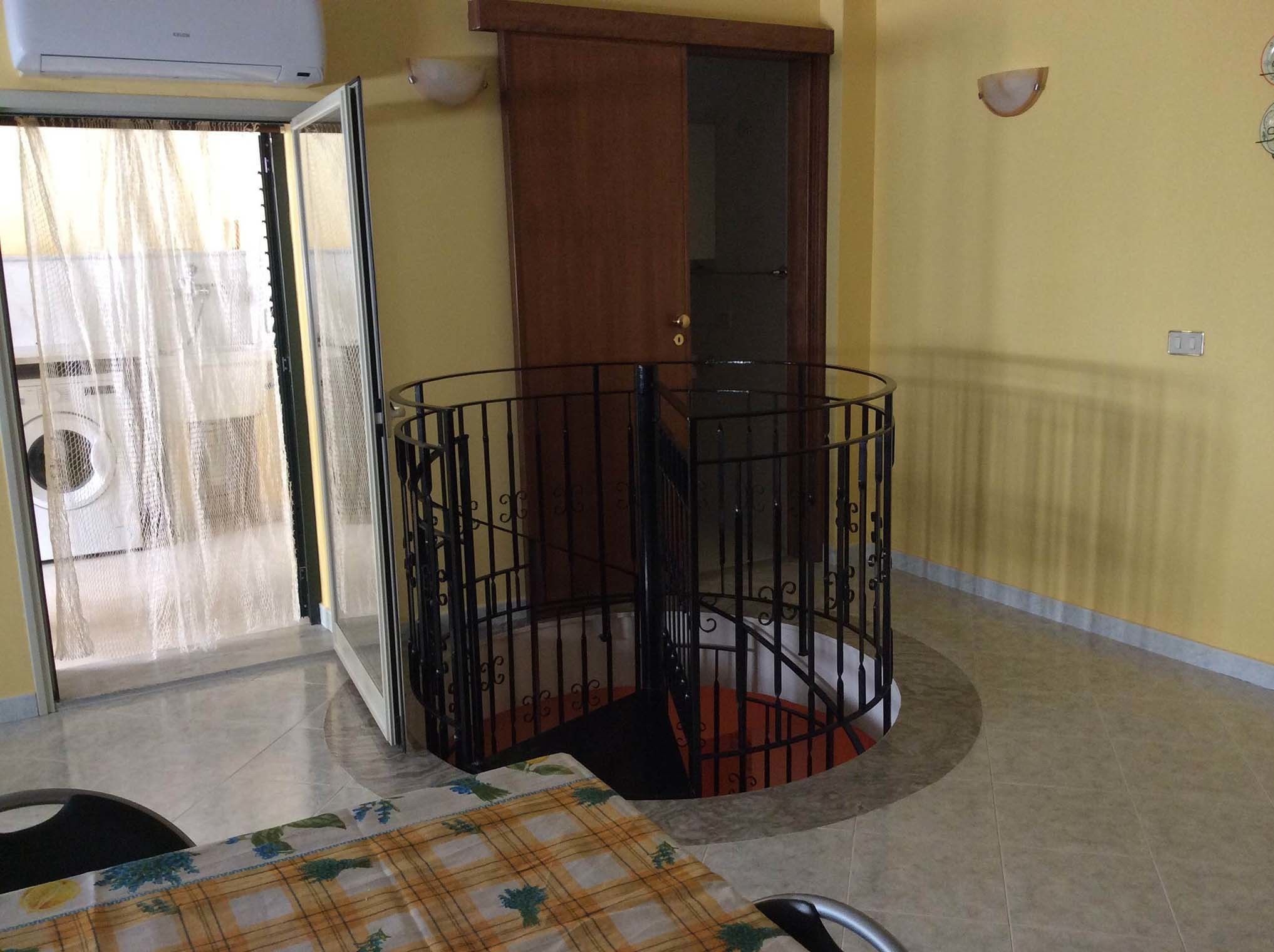 A room with a spiral staircase, a door, and a window with a curtain.