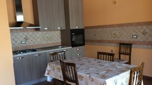 A compact kitchen with a dining area, featuring wooden cabinets, a tiled backsplash, and a table set for four. - Case Corona (Santa Flavia)