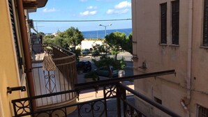 A balcony with a wrought iron railing overlooking a street with parked cars and trees. - Case Corona (Santa Flavia)
