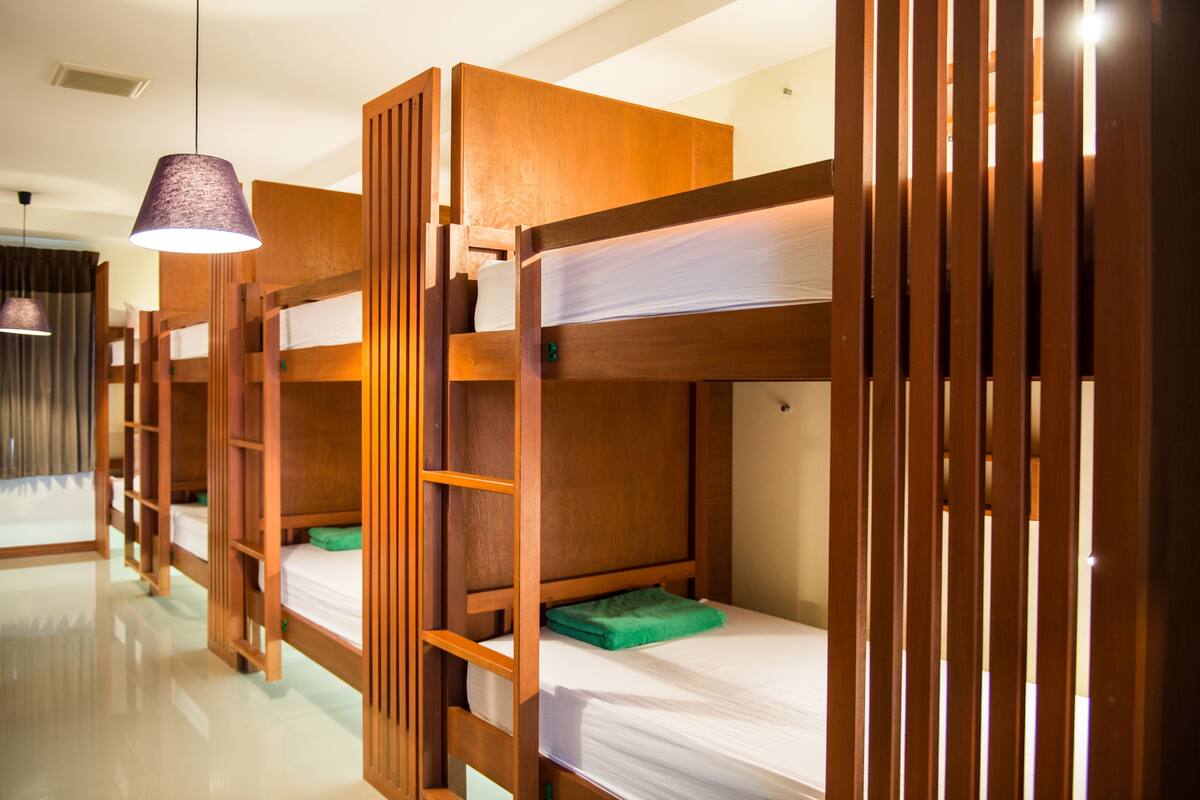 A row of bunk beds with wooden frames and white bedding, a hanging lamp, and a reflective floor.