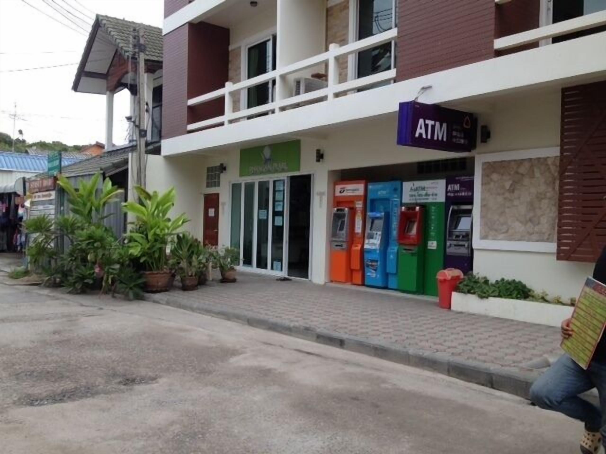 A building with an ATM on the ground floor, potted plants outside, and a sign for a business.