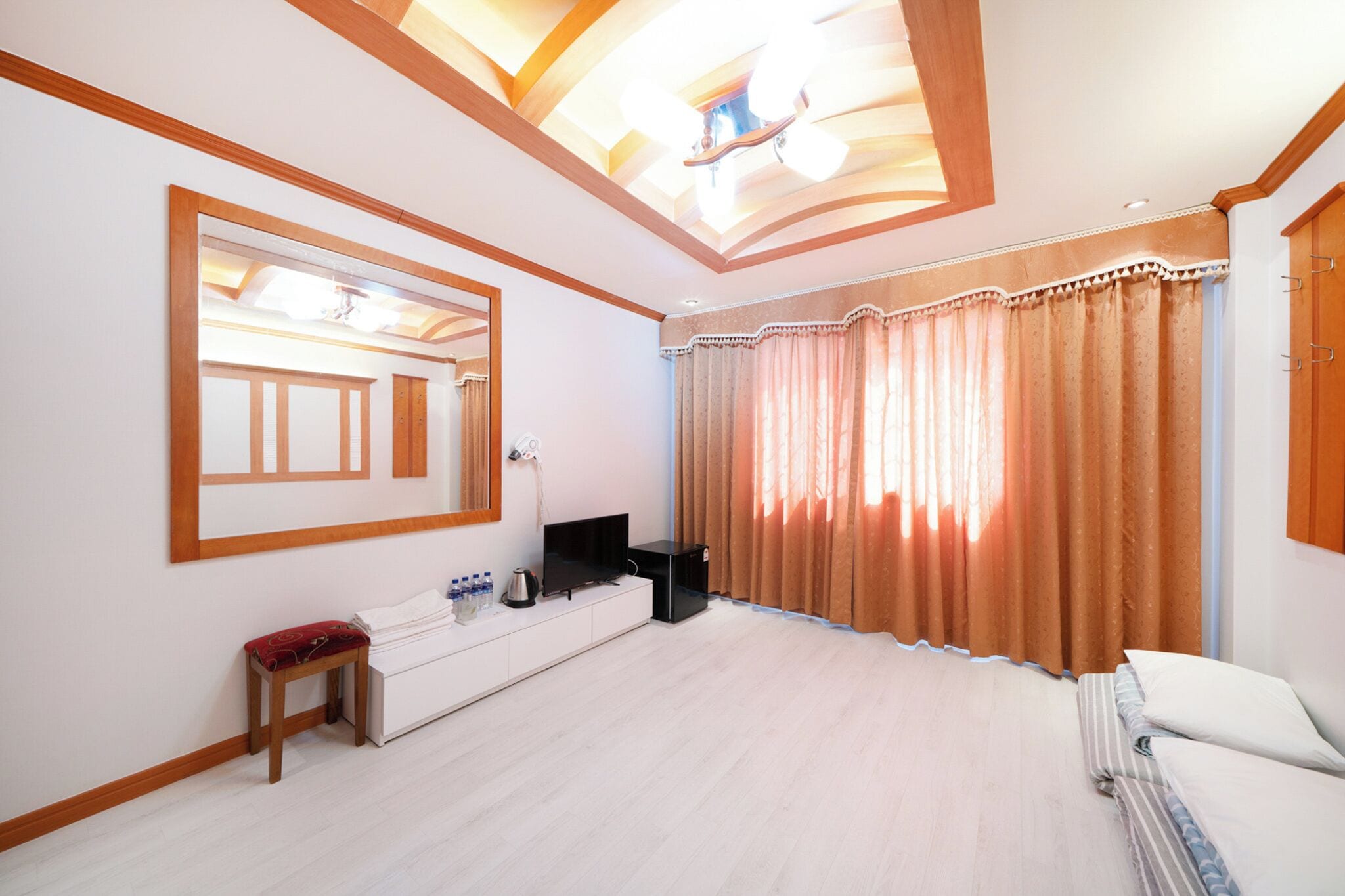 A bedroom with a large mirror, a bedside table with a lamp, a bed, and a window with curtains.