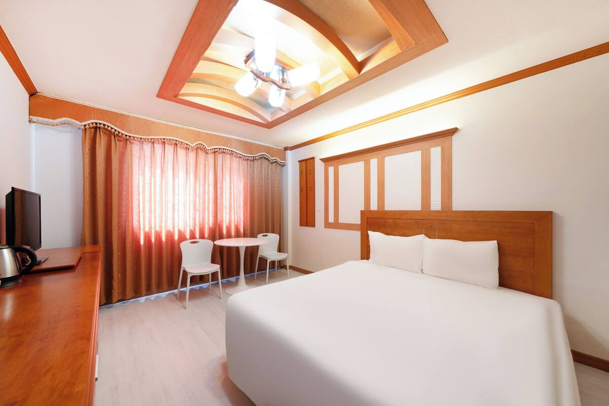 Een hotelkamer met een groot bed, een bureau met stoel, een televisie en een plafondventilator.