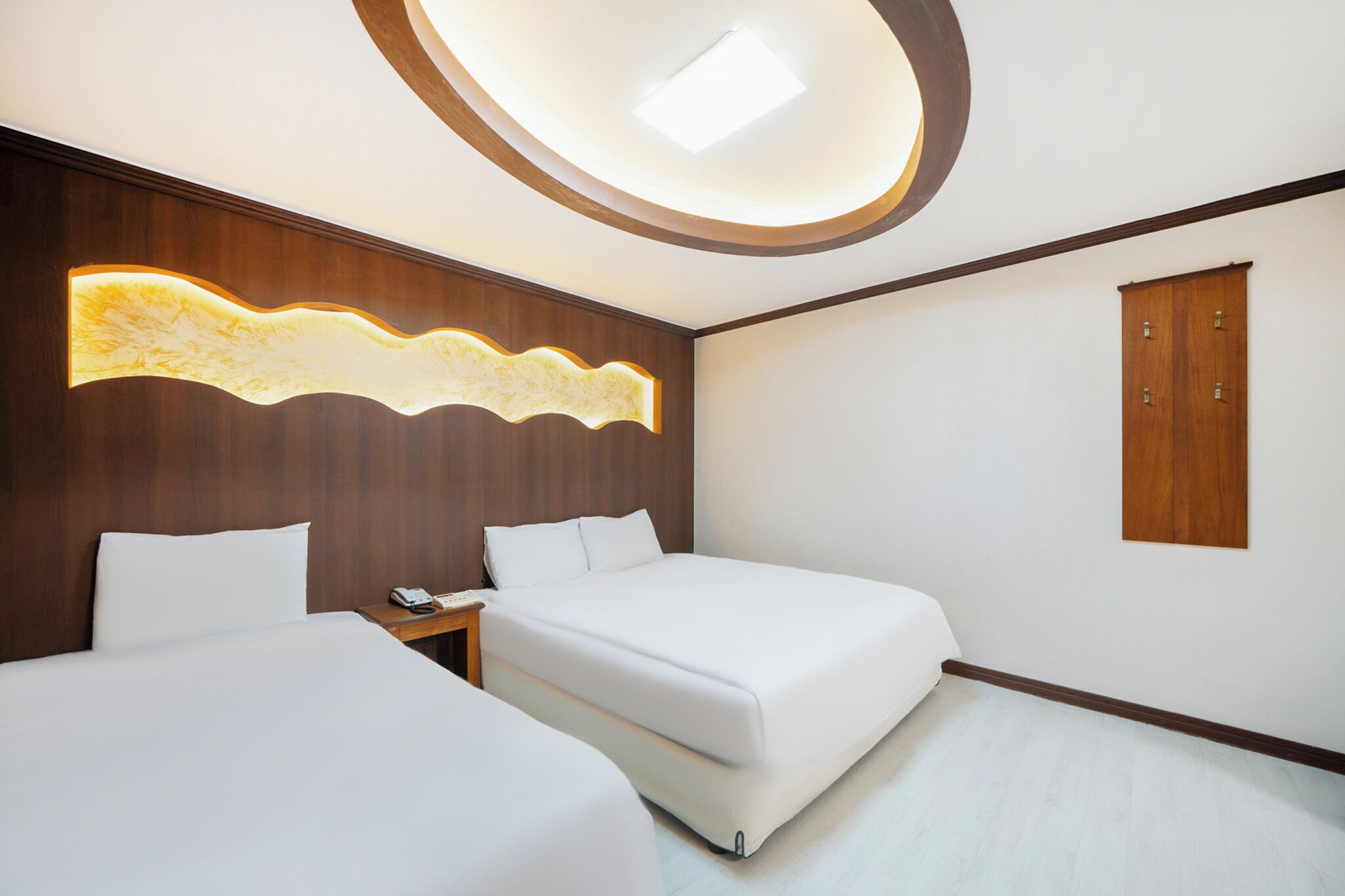 Una habitación de hotel moderna con dos camas, un panel de madera decorativo, una lámpara de techo y un armario de madera.