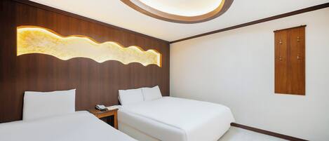 Una habitación de hotel moderna con dos camas, un panel de madera decorativo, una lámpara de techo y un armario de madera.