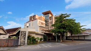 A modern building with a large glass entrance, a stone facade, and a tree in front. - Palette Grand Sae Boutique Hotel (Surakarta)
