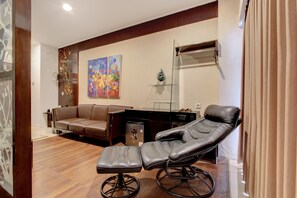 A room with a leather sofa, a reclining chair, a small table, and a painting on the wall. - Palette Grand Sae Boutique Hotel (Surakarta)