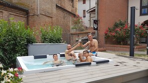 A hot tub with four people, surrounded by greenery and a brick building. - Locanda San Giacomo (Agliano Terme)