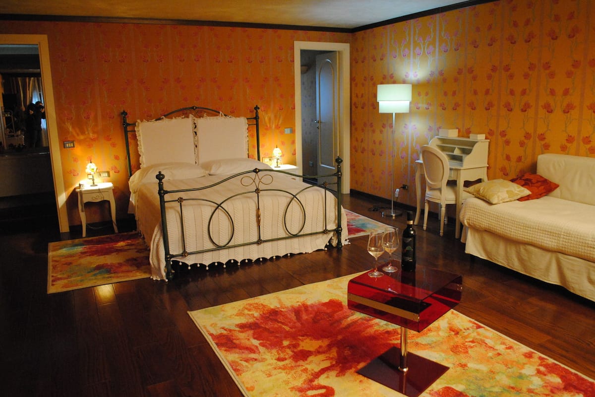 A bedroom with a bed, bedside tables, a desk, a chair, and a sofa.