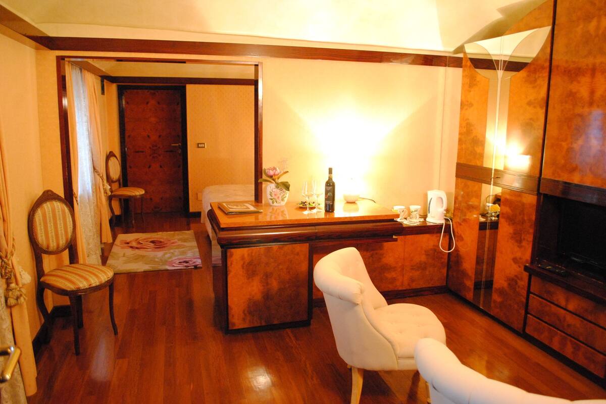 A hotel room with a wooden floor, a dining area with a table and chairs, a TV, and a fireplace.