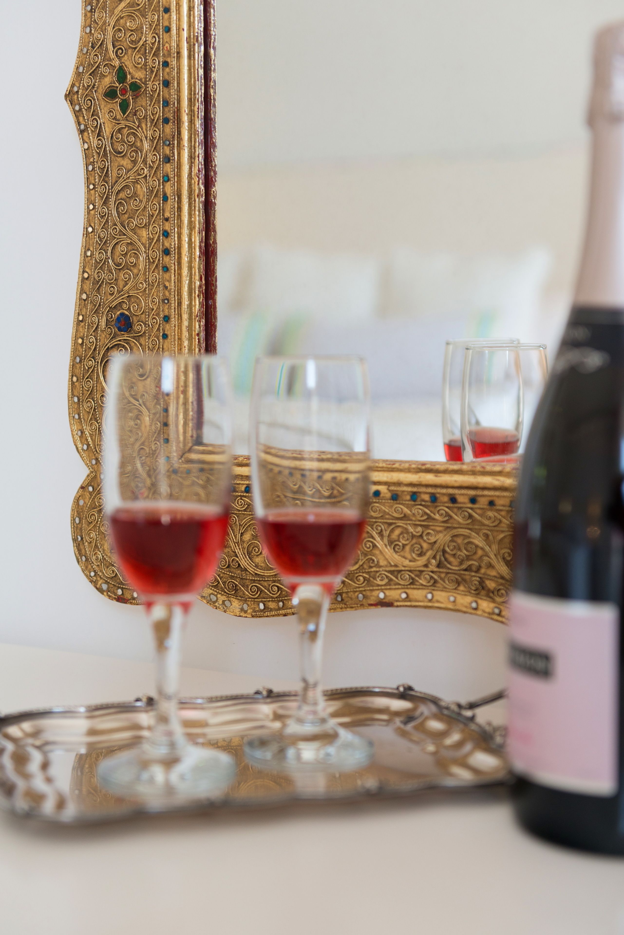 A table with two wine glasses and a bottle of wine, set against a gold-framed mirror.