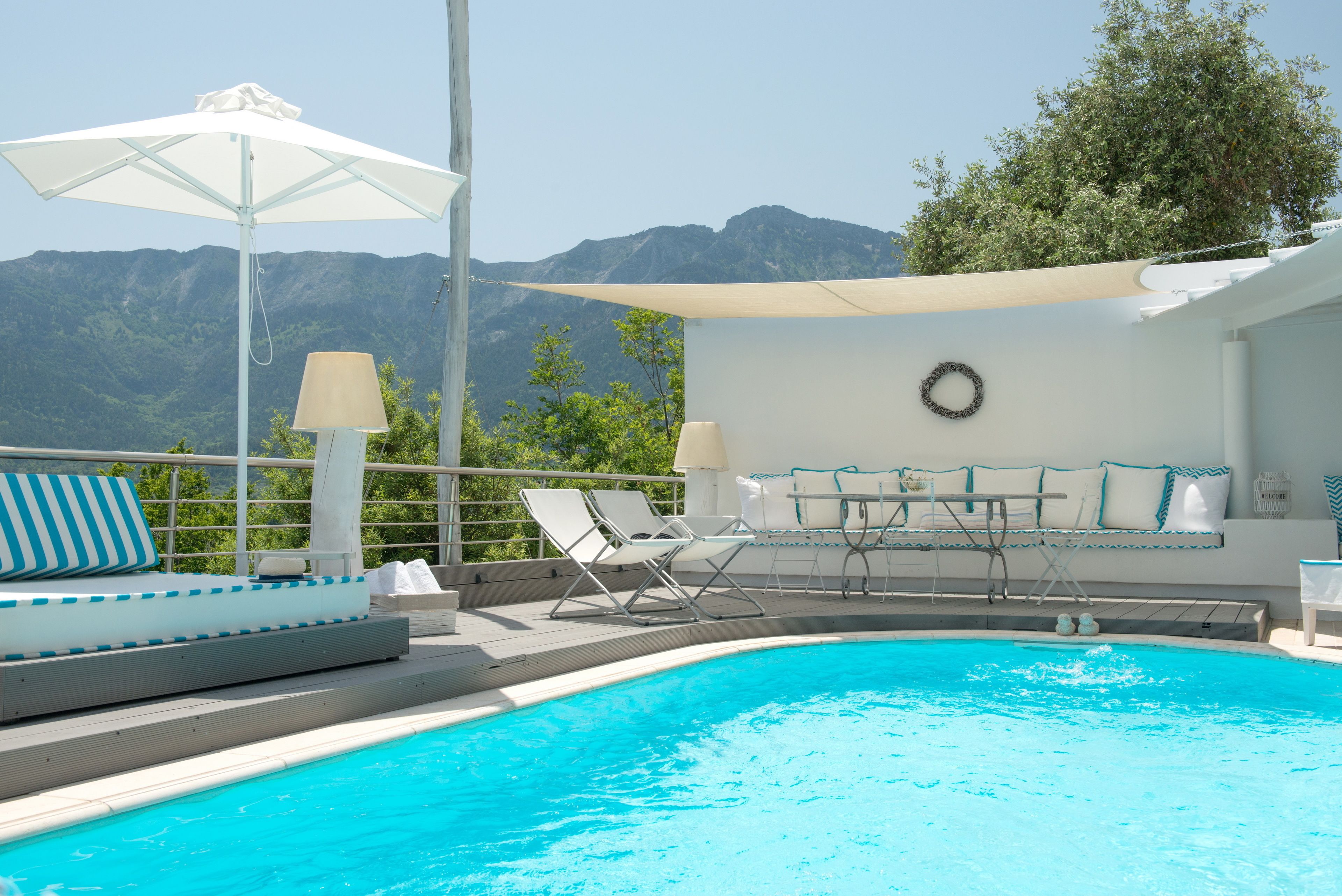 A pool area with lounge chairs, a table, and umbrellas, overlooking a mountainous landscape.
