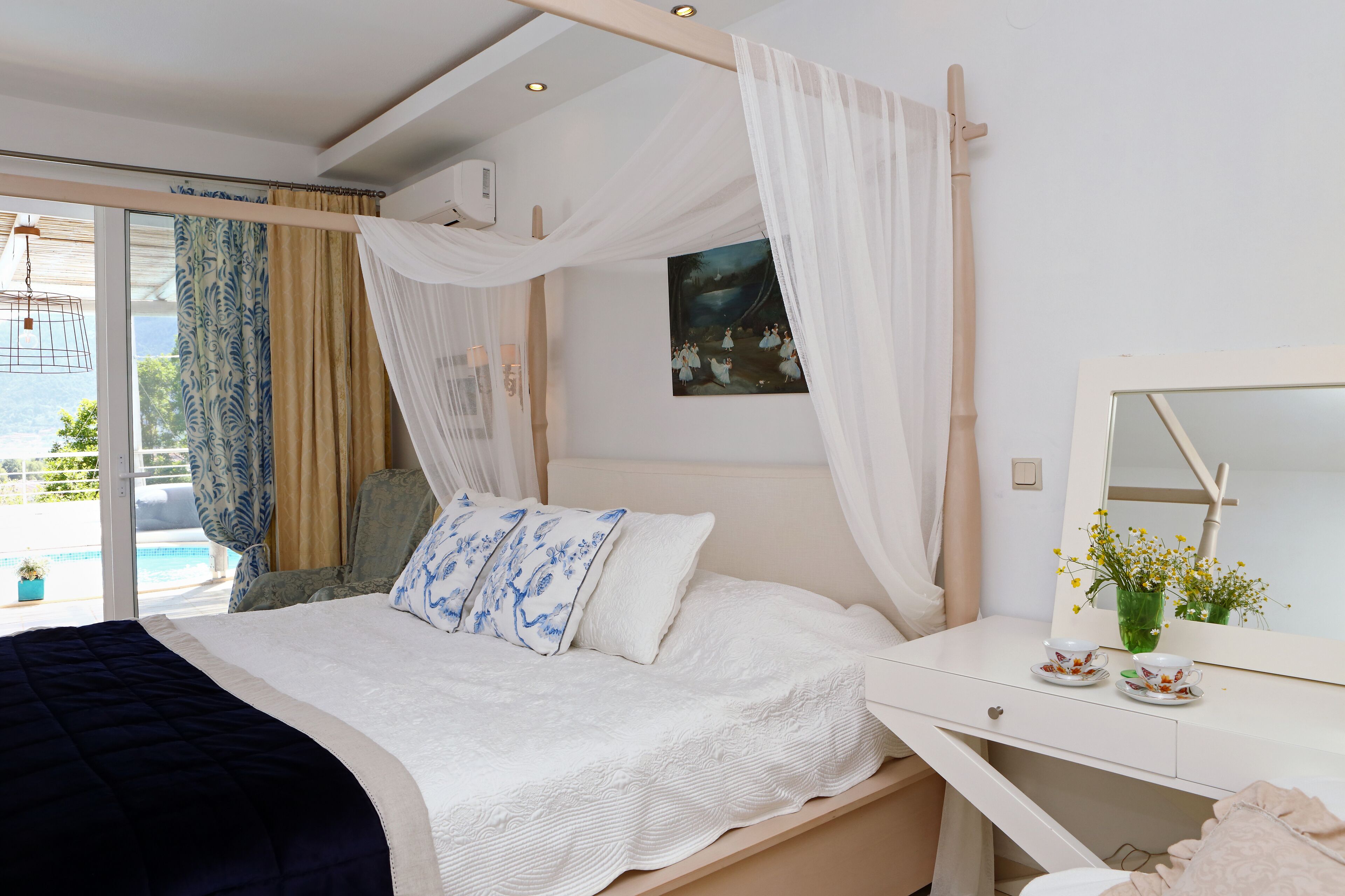 Une chambre à coucher avec un lit, une table de chevet dotée d’un miroir, une fenêtre avec des rideaux et une vue sur l’extérieur.