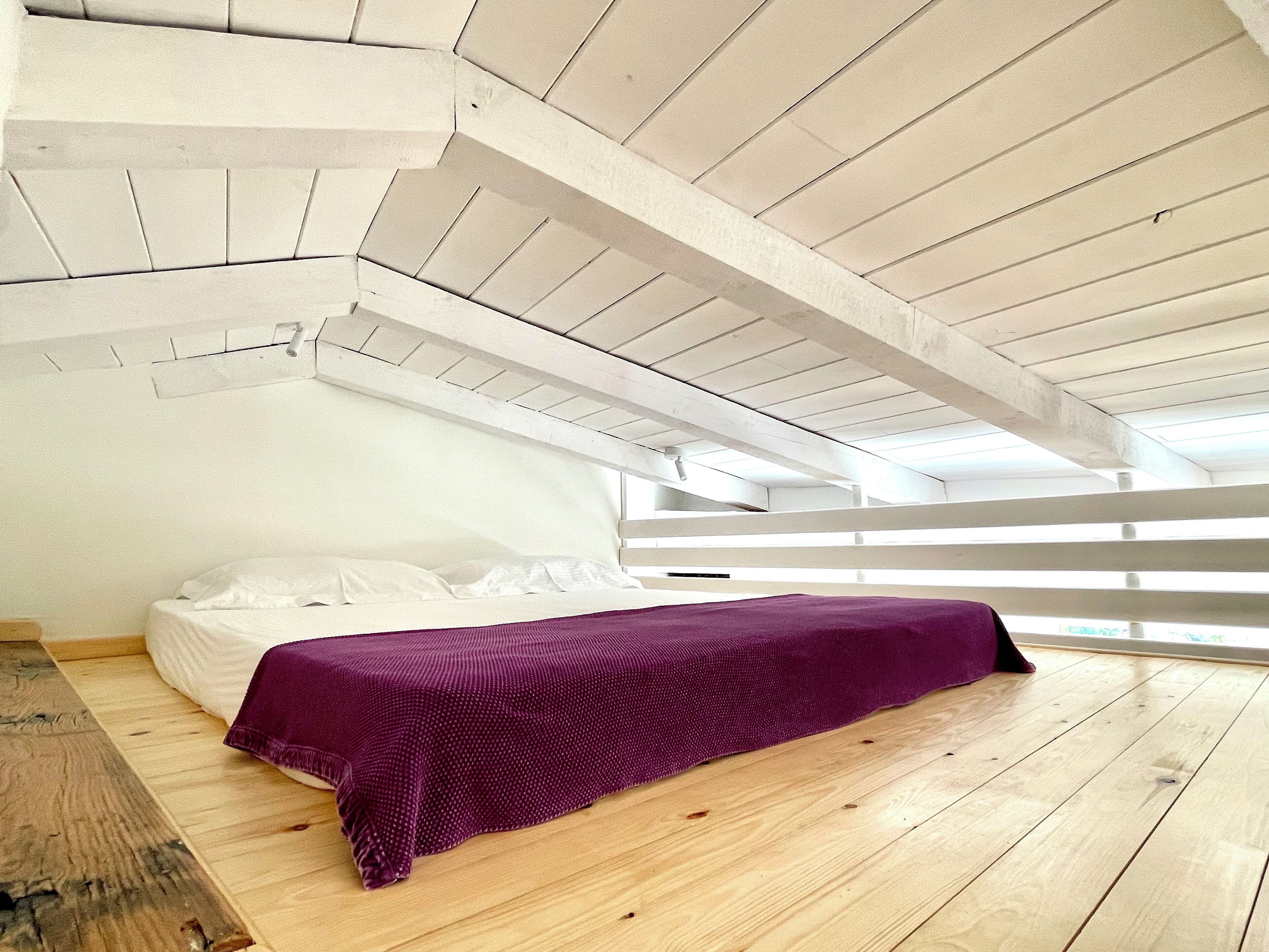 Un dormitorio con piso de madera, paredes blancas y techo inclinado.
