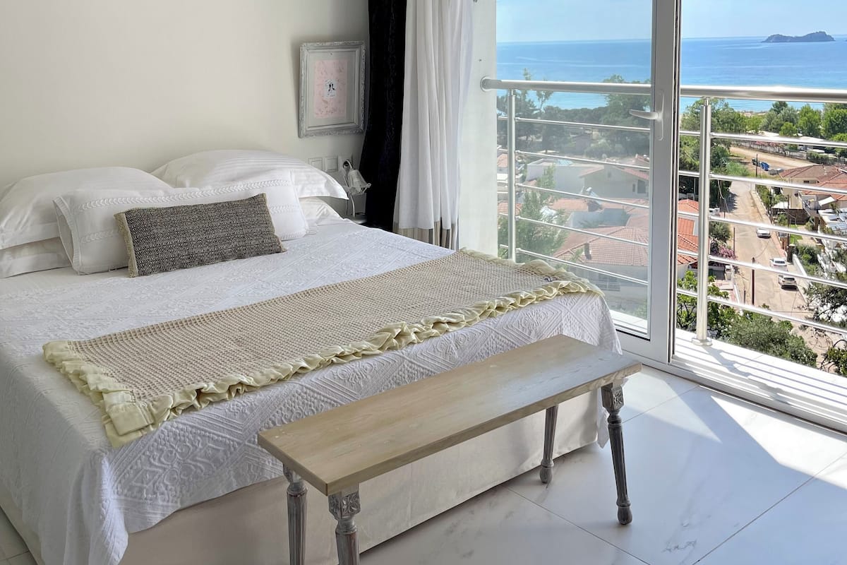A bedroom with a large bed, a bedside table, and a view of the sea.