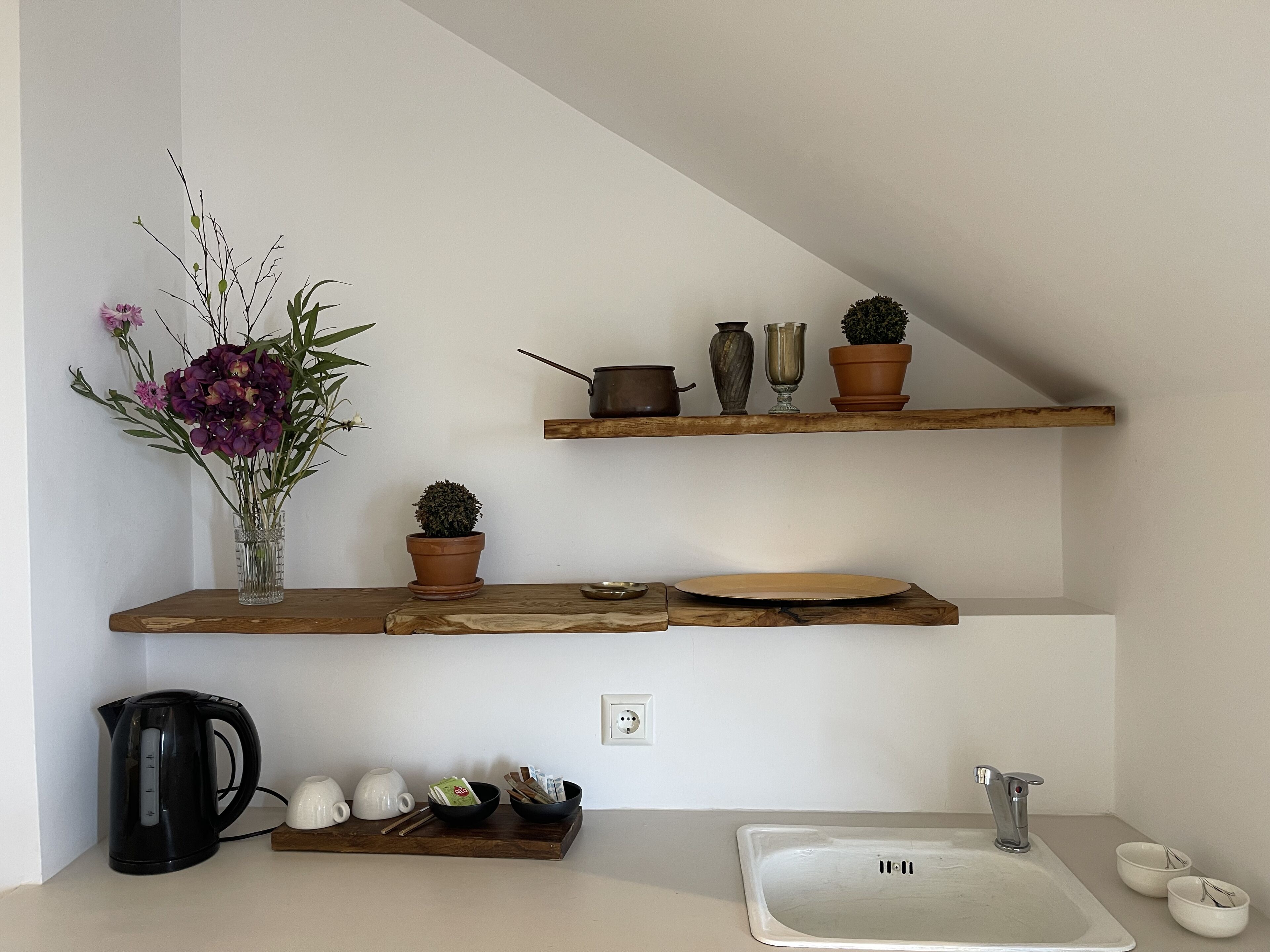A kitchen with wooden shelves holding various items, a coffee maker, and a sink.