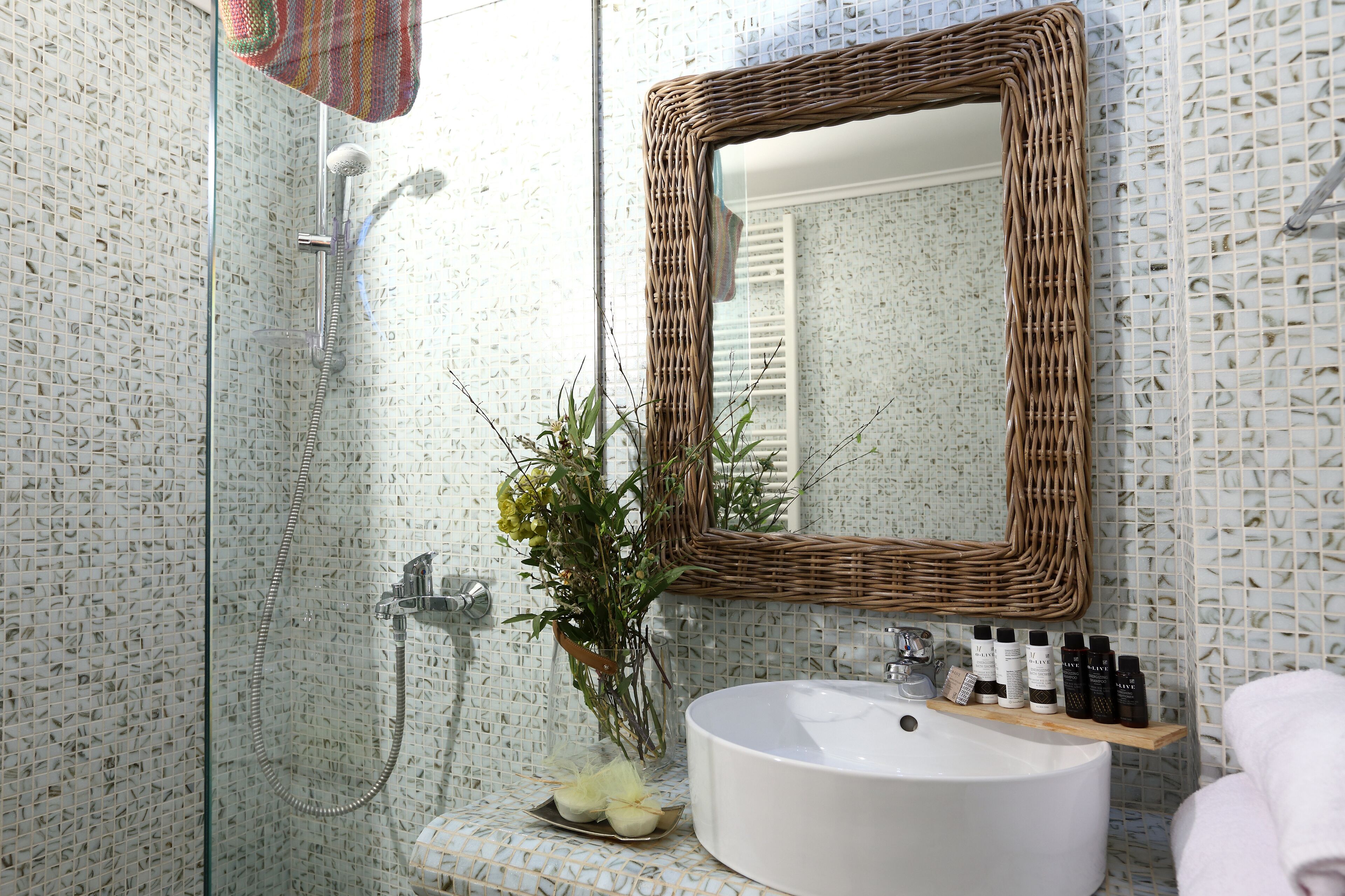 A bathroom with a glass-enclosed shower, a white sink, a wicker mirror, and a shelf with toiletries.