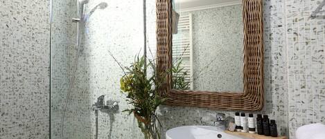 Un bagno con doccia vetrata, un lavandino bianco, uno specchio in vimini e uno scaffale con articoli da toilette.
