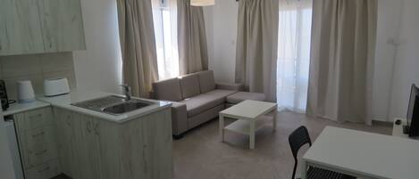Un apartamento moderno con cocina, comedor y sala de estar. Incluye una kitchenette, una mesa de comedor con sillas, un sofá y dos lámparas colgantes.