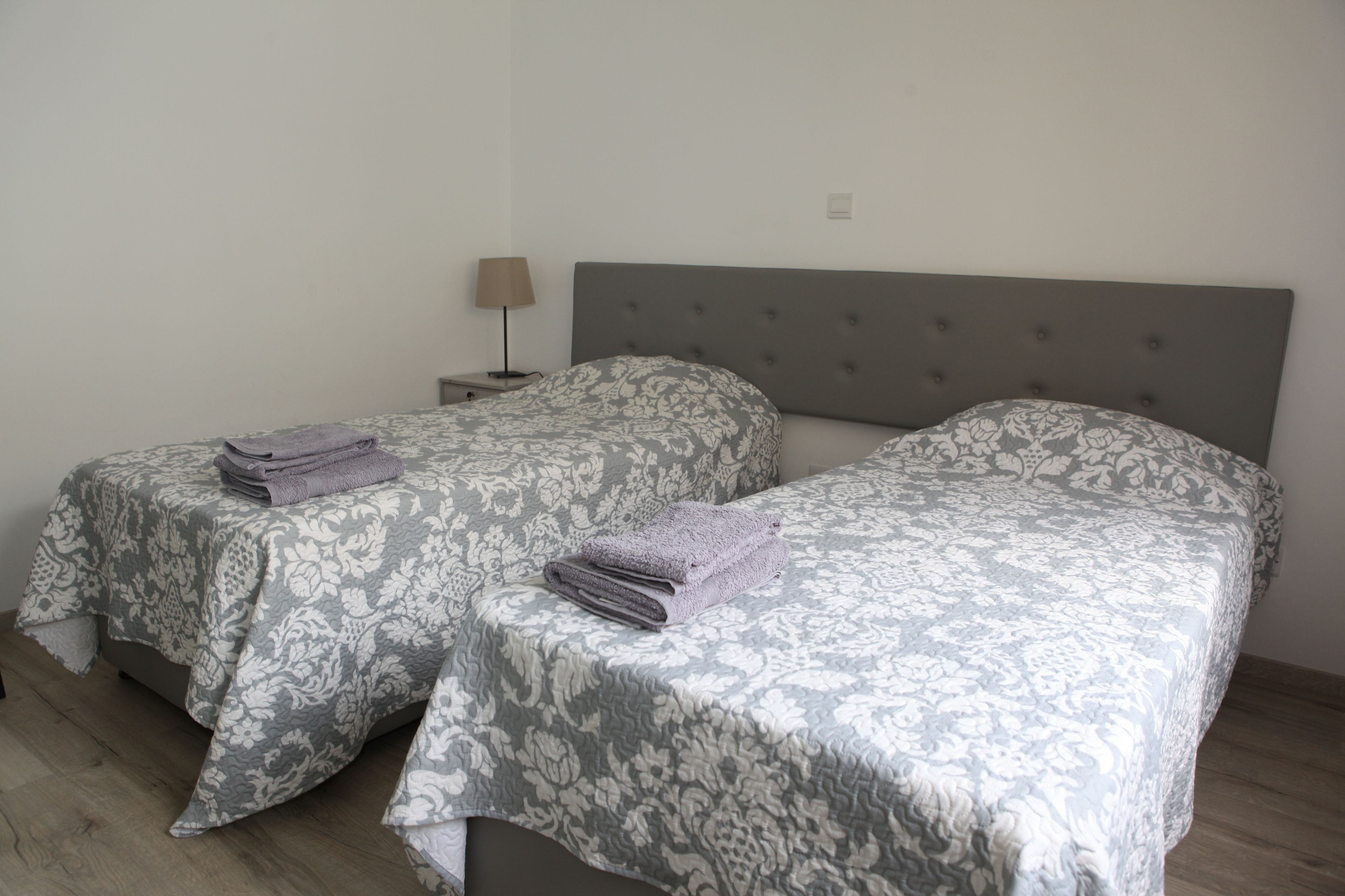 Two twin beds with patterned bedding, a nightstand with a lamp, and a neutral-colored headboard.