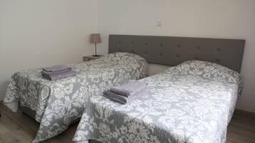 Two twin beds with patterned bedding, a nightstand with a lamp, and a neutral-colored headboard.