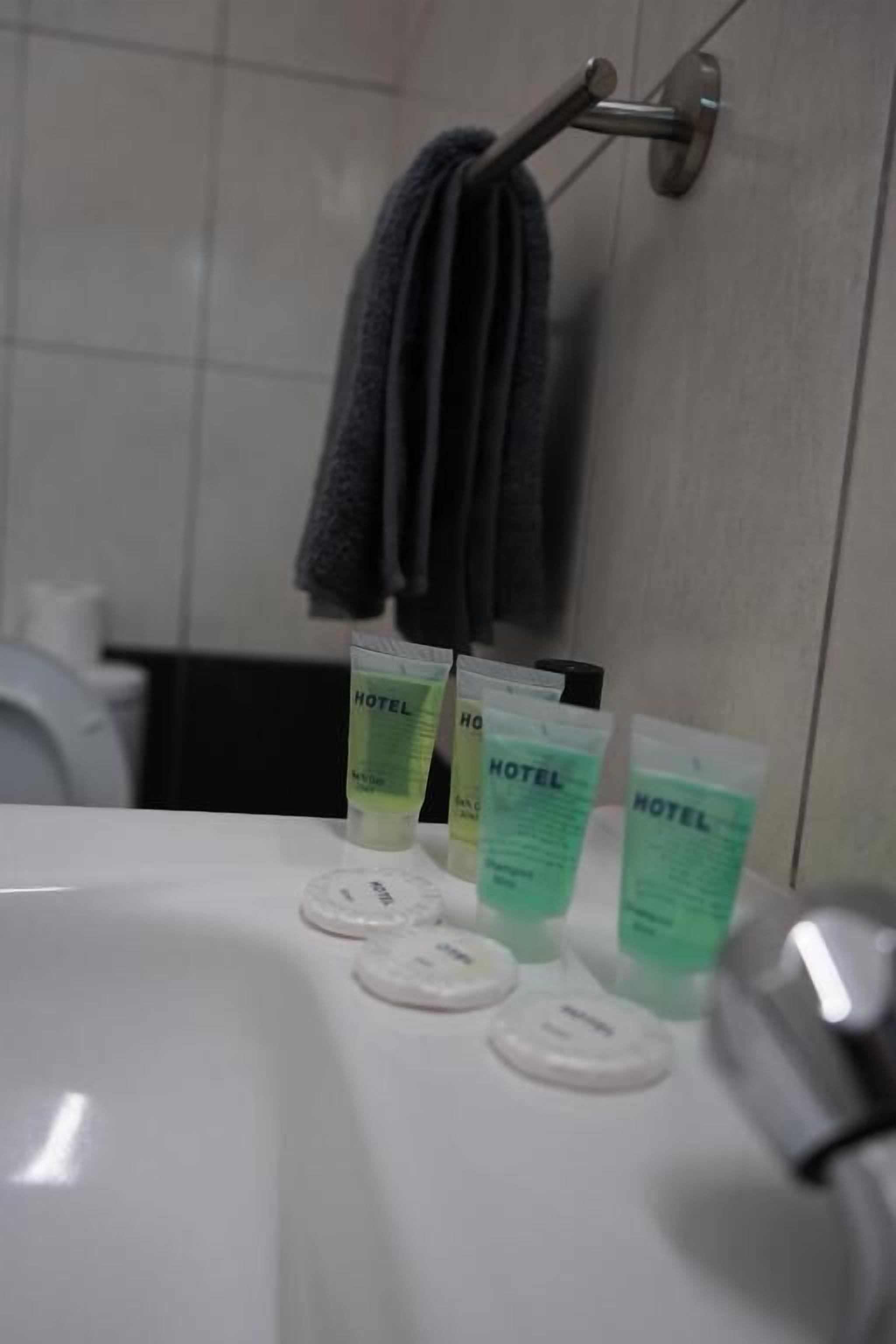 A bathroom with a white sink, three green hotel lotion tubes, and a towel hanging on a metal rack.