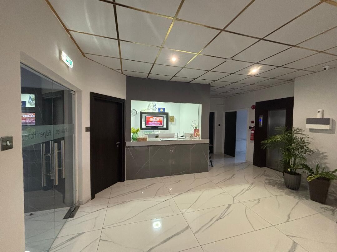 Un vestíbulo de hotel con mostrador de recepción, puerta de cristal de entrada y suelo de baldosas.