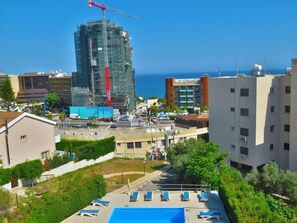 Vista de una obra en construcción con una grúa, una piscina con tumbonas y edificios circundantes.