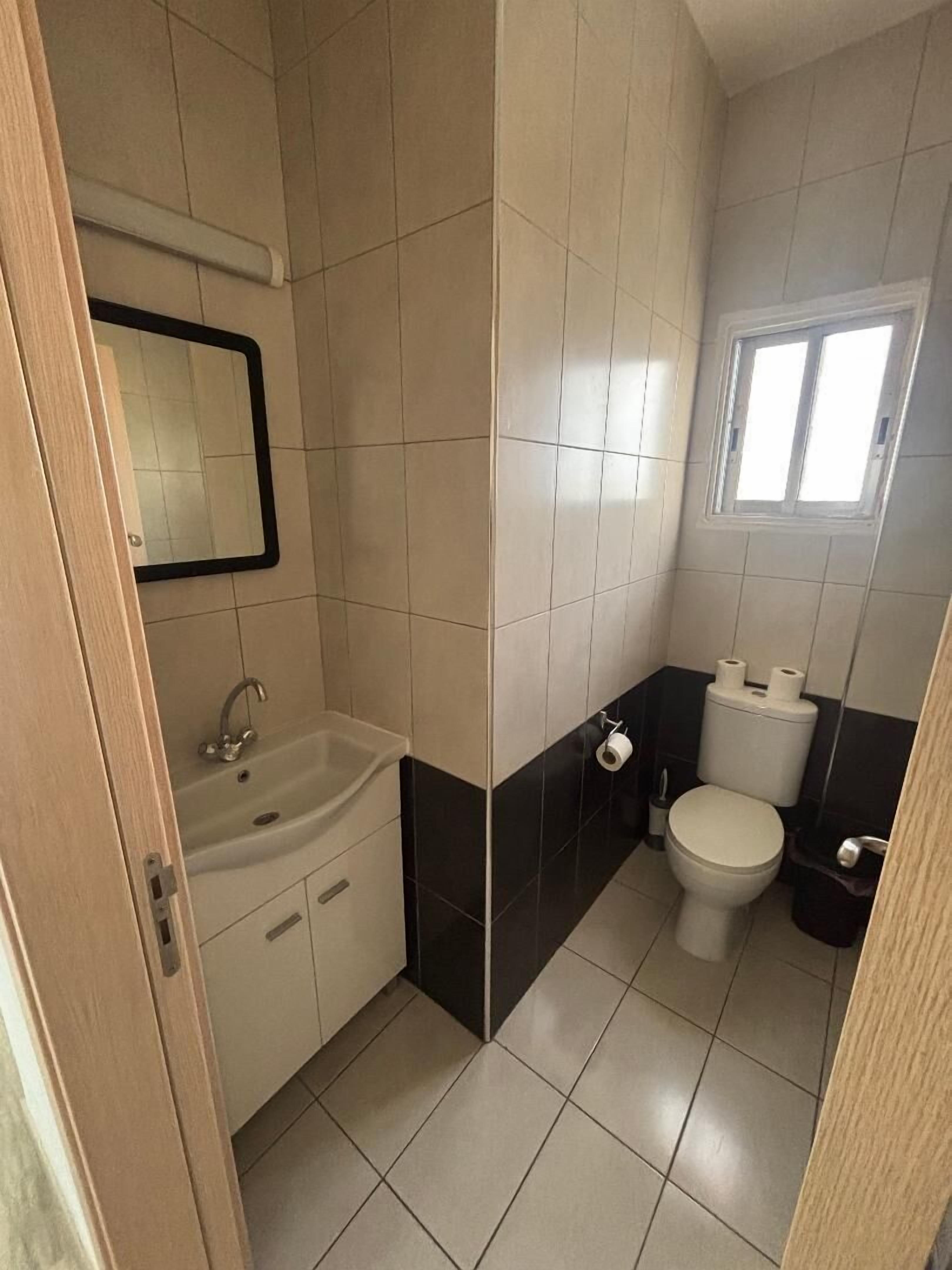 A small bathroom with a sink, mirror, toilet, and a window.