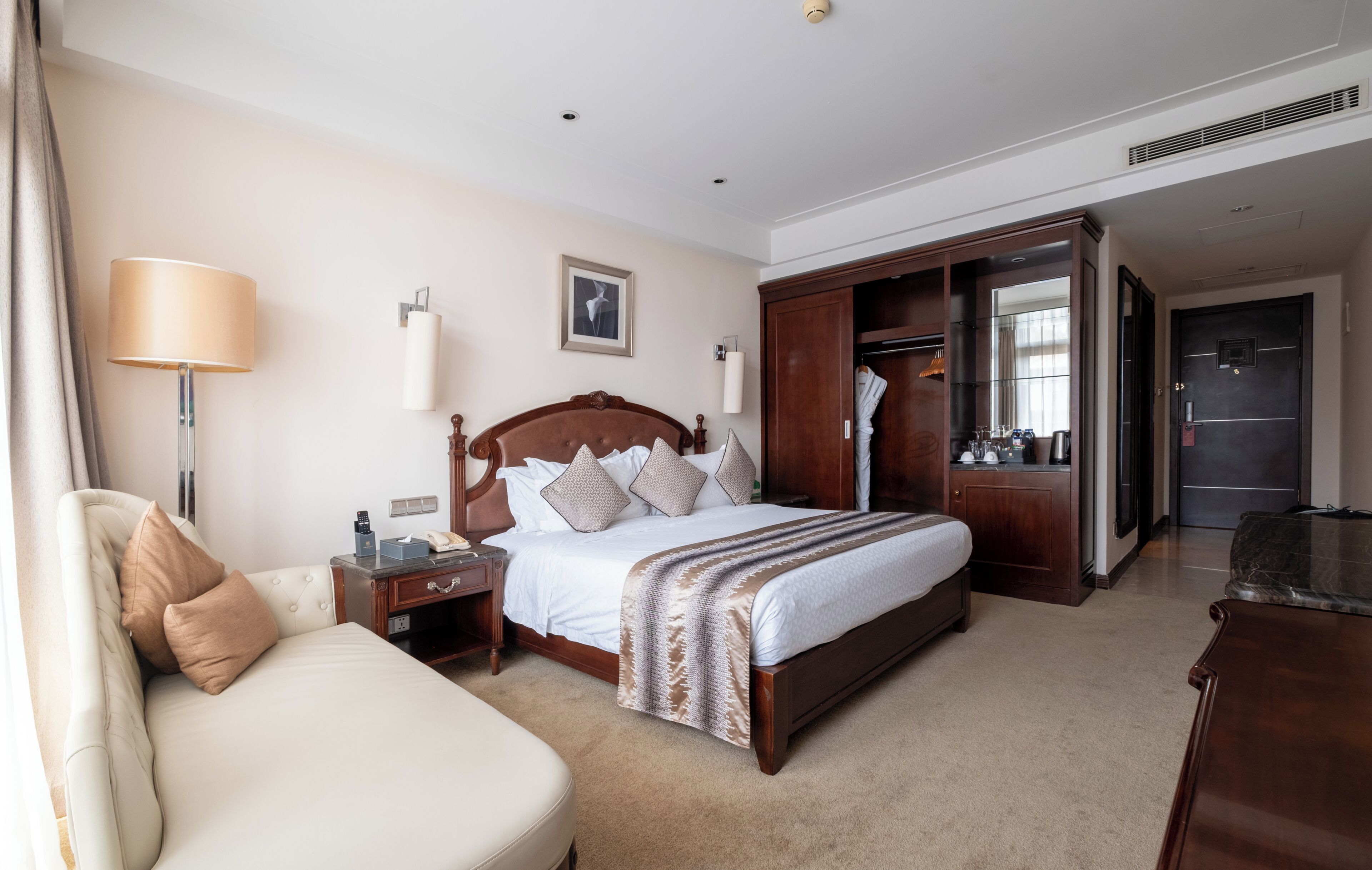 Una habitación de hotel con cama, mesita de noche, lámpara, armario y escritorio con silla.