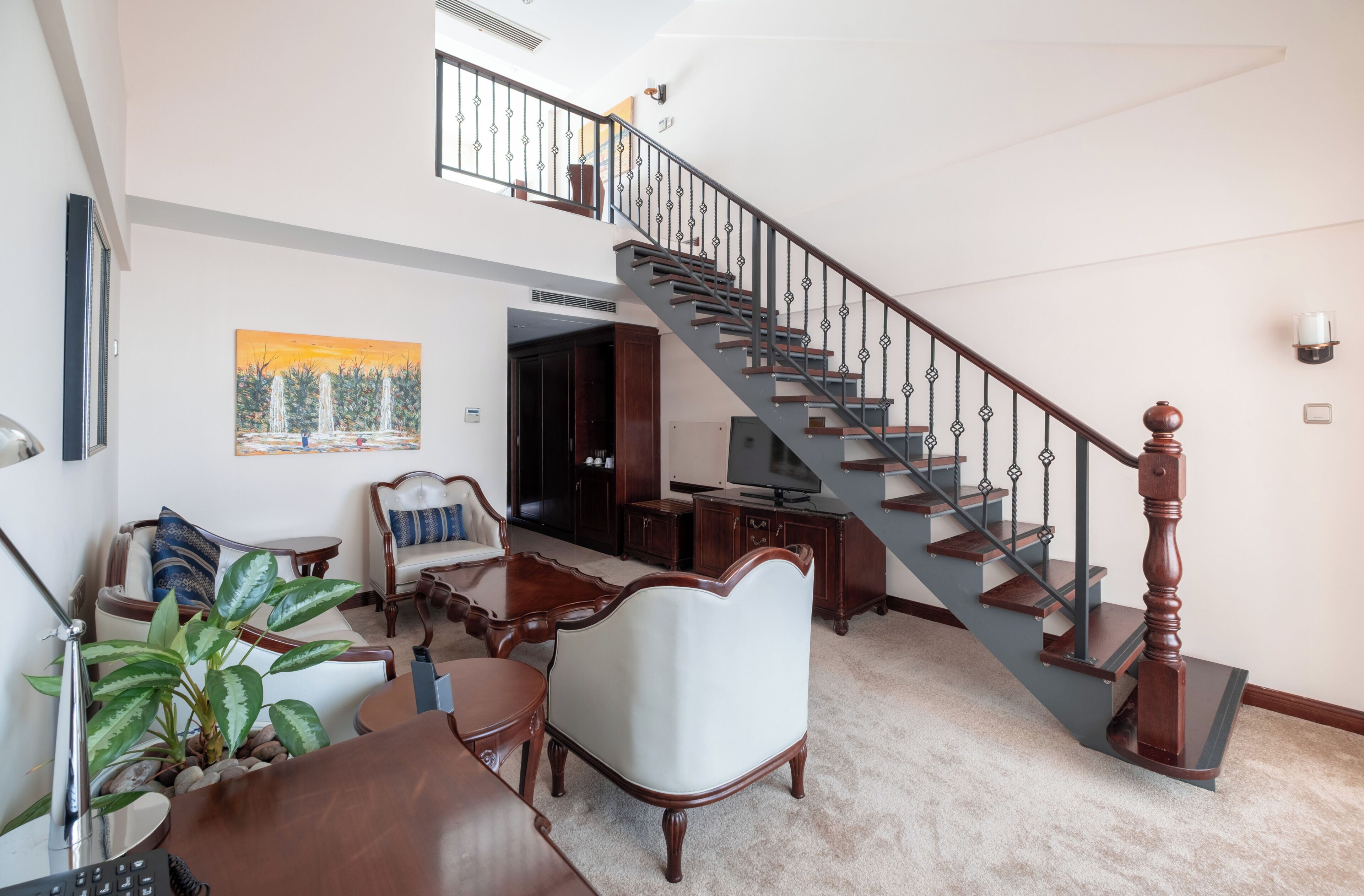 A staircase with a wooden handrail and metal balusters, a dining area with a table and chairs, and a painting on the wall.