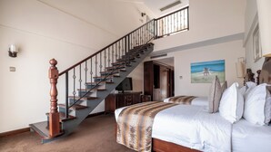 Un dormitorio con cama de madera, una escalera con barandilla de metal, un cuadro en la pared y un televisor en una esquina.