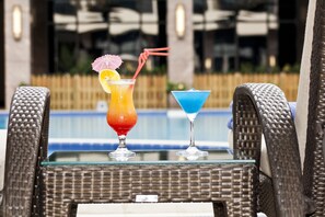 Deux fauteuils en osier, séparés par une table en verre, chacun portant un cocktail agrémenté d’une paille et d’une garniture.