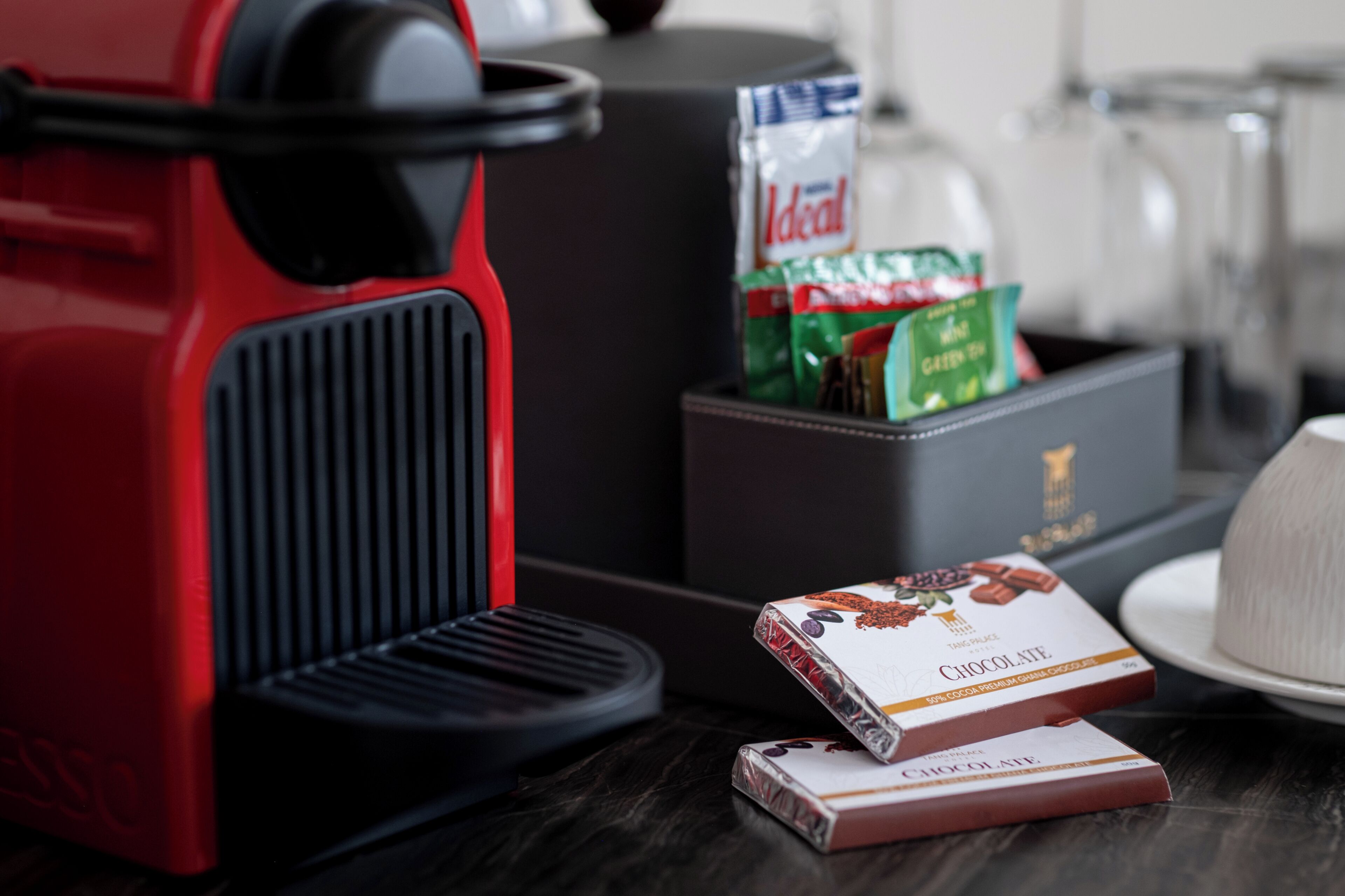 Une cuisine avec une machine à café rouge, une boîte de chocolats et un paquet de café.