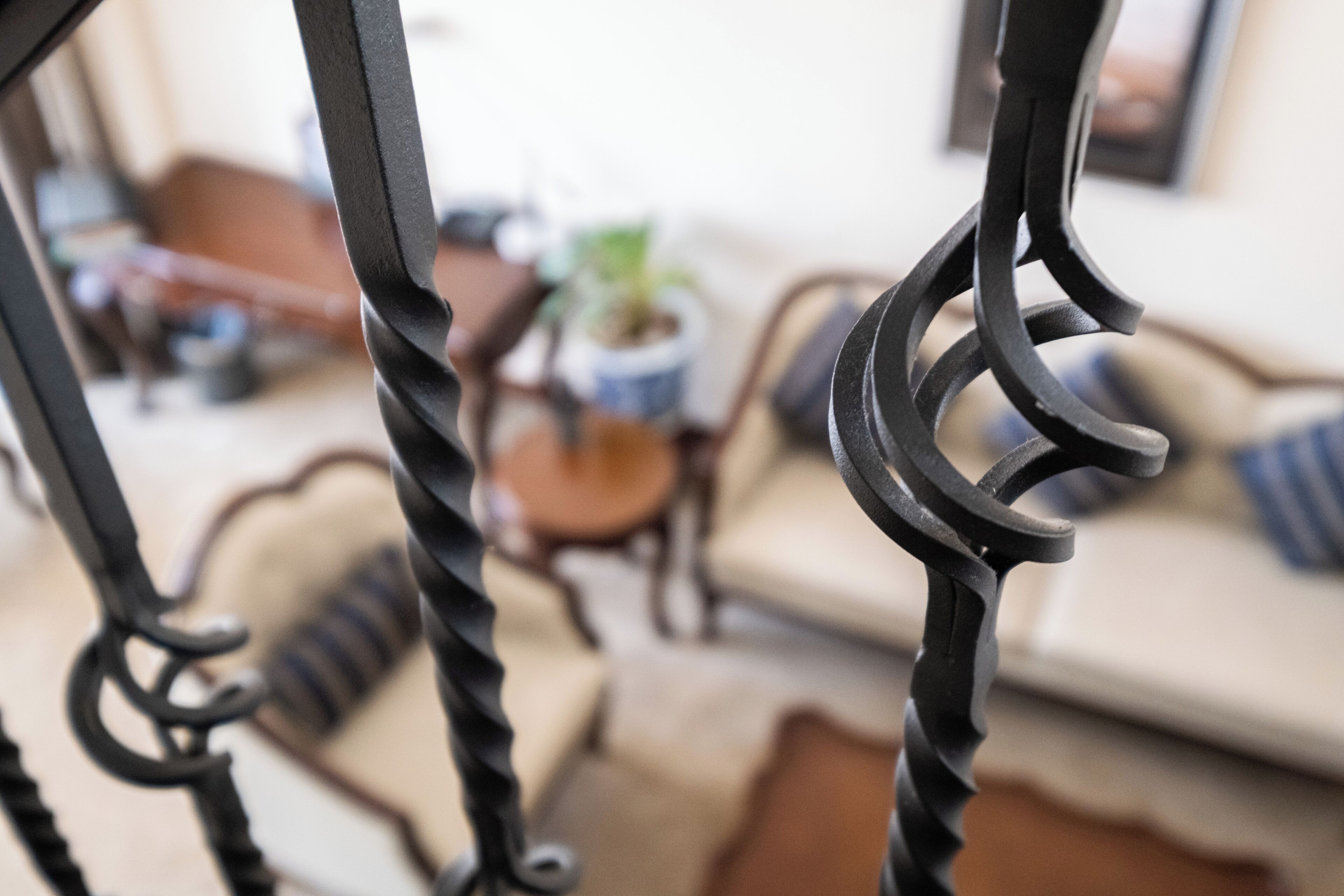 A close-up of a metal railing with a blurred background featuring a sofa and a small table with a plant.