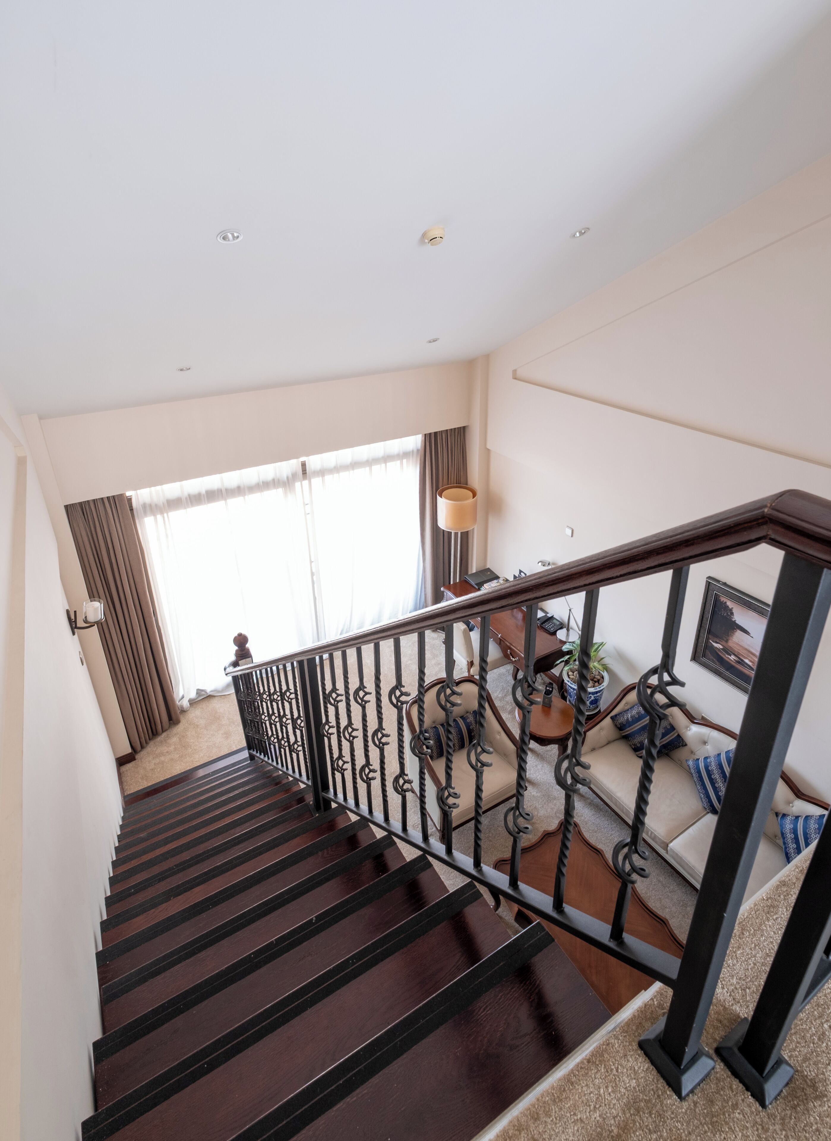 Una escalera con barandilla de madera oscura y balaustres negros, que lleva a una sala de estar con un sofá y una mesa.