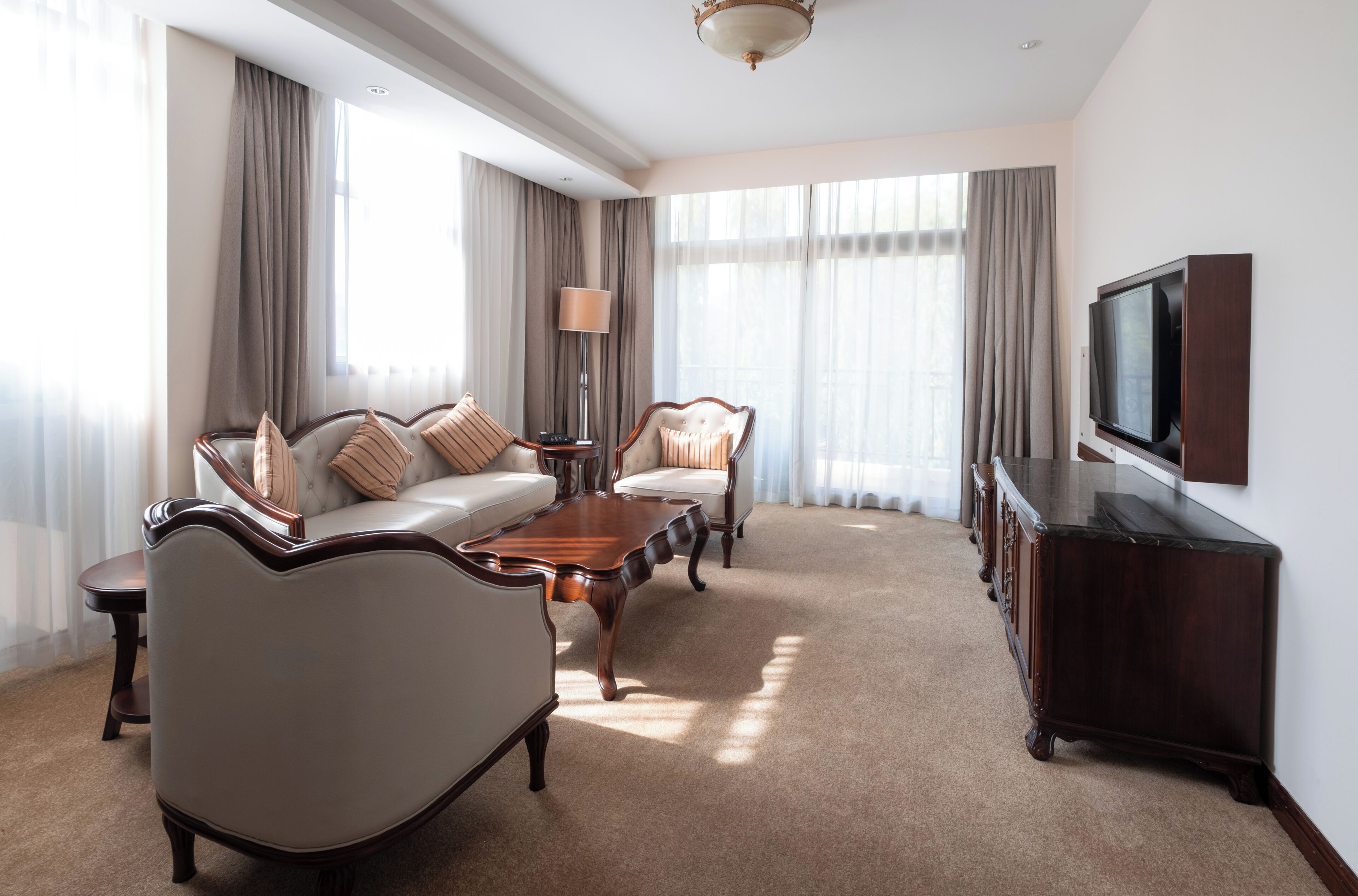 A hotel room with a sofa, armchairs, a coffee table, a TV, and a dresser.